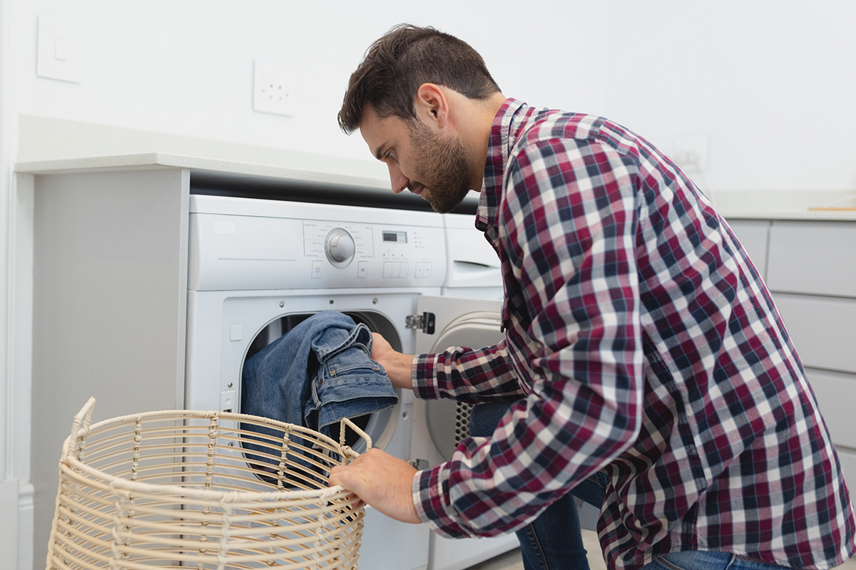 Side view of Caucasian man putting dirty clothes into the washing machine in a comfortable home
